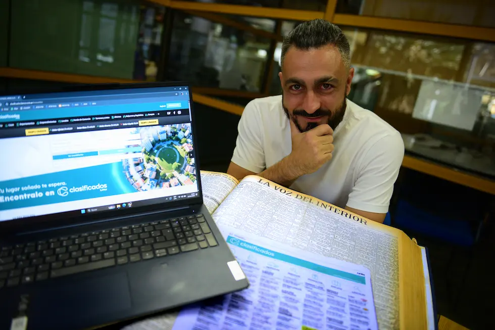Matías Merguerian junto a un tomo encuadernado de los clasificados de La Voz del Interior y la versión digital en pantalla